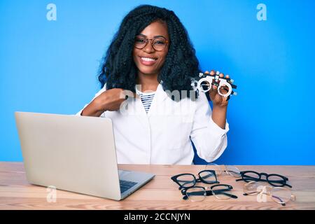 Bella donna africana che tiene gli occhiali di optometria che punta il dito ad uno sorridente felice e orgoglioso Foto Stock