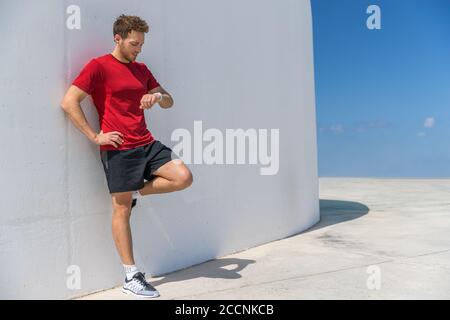 Il runner man di smartwatch controlla i progressi dell'orologio sportivo Smart fitness durante l'allenamento cardiofitness break. Un atleta che si rilassa utilizzando l'app online Foto Stock