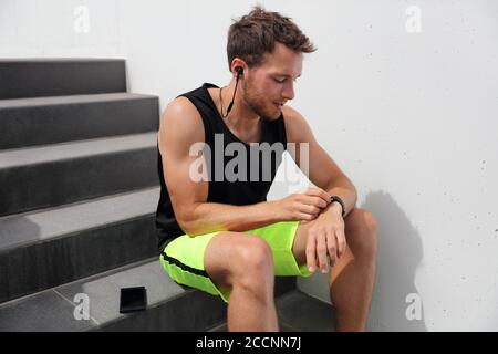 Il runner man di smartwatch controlla i progressi dell'orologio sportivo Smart fitness durante la pausa di corsa dopo l'allenamento cardio hiit per le scale. Atleta che usa Foto Stock