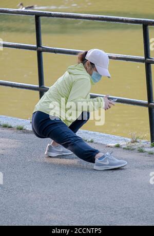 MULTITASKING. Una donna controlla il suo telefono cellulare mentre contemporaneamente allunga i muscoli delle gambe prima di un allenamento. A Flushing, Queens, New York City. Foto Stock