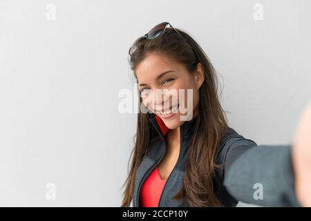 Donna asiatica che scatta foto ritratto selfie dello smartphone. Carina ragazza felice sorridente alla macchina fotografica che scatta le foto di se stessa su sfondo bianco a casa Foto Stock