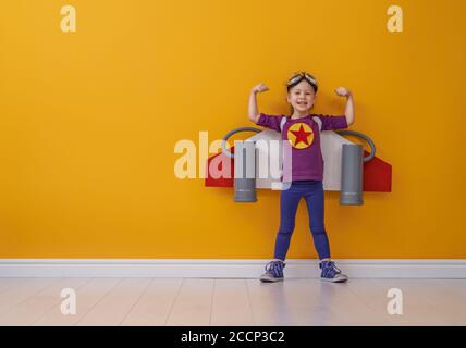 Bambina in costume astronauta sta giocando e sognando di diventare uno spaceman. Ritratto di capretto divertente su uno sfondo di parete gialla. Foto Stock