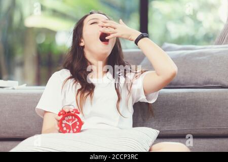 Donna asiatica che spegne la sveglia mentre dormivo durante le vacanze. La ragazza sta avendo problemi svegliarsi tardi di mattina. Foto Stock