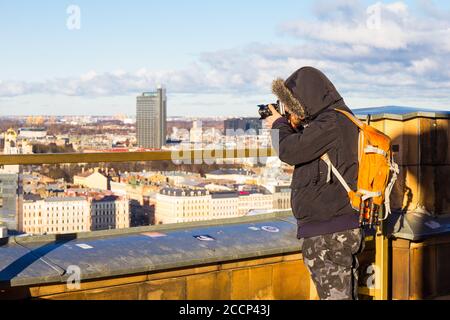 Fotografo con borsa grande per scattare foto simbolo dell'antica città europea da un punto di vista alto. Accademia delle Scienze lettone. Giorno invernale soleggiato Foto Stock
