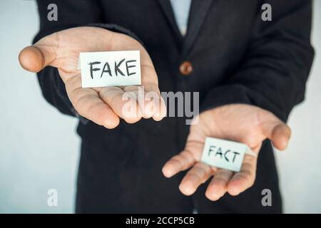 falso e fatto dell'iscrizione sulle tavole nelle mani di un uomo. Il concetto di scegliere la verità o la menzogna. Un tentativo di inganno, manipolazione di Foto Stock