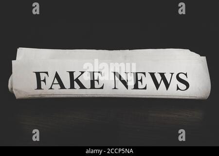 concetto di falsa notizia. Giornale Fake News alla scrivania in ufficio. Giornale arrotolato su sfondo scuro Foto Stock