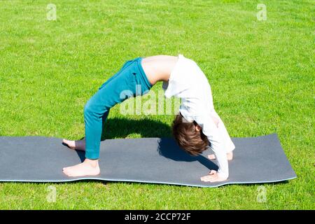 Il ragazzo pratica yoga sull'erba. Attività all'aperto per bambini Foto Stock