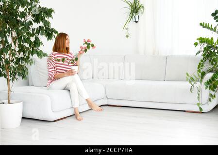 ragazza con una pianta in una pentola. Sorridente vera donna a casa. Interno bianco. Spazio di copia Foto Stock