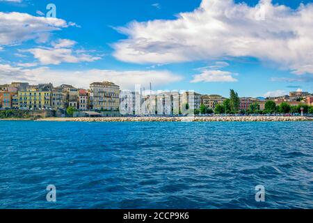 Isola di Corfù/Grecia - 7 maggio 2019: Paesaggio urbano di Kerkyra - baia di mare con acque turchesi calme, vecchie case colorate, cielo blu con nuvole bianche e colline su Foto Stock