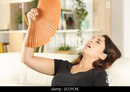 Ragazza che soffre colpo di calore che si accanisce seduta su un divano dentro il soggiorno a casa Foto Stock