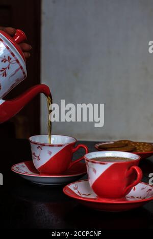 Versare il tè in una tazza di ceramica su un tavolo di legno con un po' di biscotto sul piatto. Messa a fuoco parziale. Foto Stock