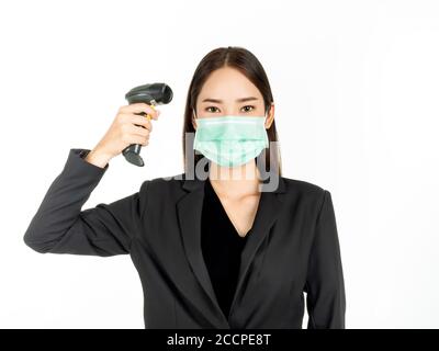 Donna asiatica che indossa una maschera medica verde con termometro a infrarossi o termometro digitale isolato su sfondo bianco. Donna d'affari in tuta ai Foto Stock