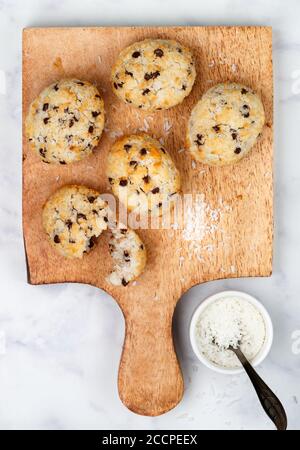 Biscotti fatti in casa appena sfornati (biscotti) con gocce di cocco e cioccolato su una tavola di legno su sfondo di marmo. Delizioso dessert croccante per Brea Foto Stock