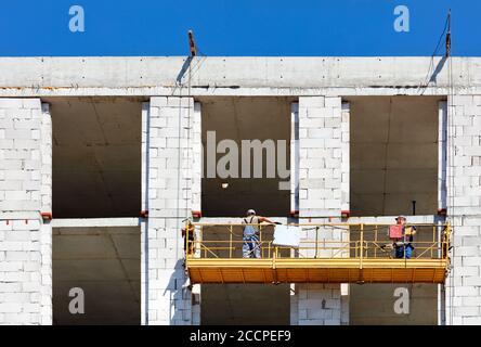 Culla da costruzione con i lavoratori sulla parete di una casa in costruzione, la piattaforma elettrica sospesa è affidabile per lavori sicuri in altezza. Foto Stock
