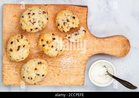 Biscotti fatti in casa appena sfornati (biscotti) con gocce di cocco e cioccolato su una tavola di legno su sfondo di marmo. Delizioso dessert croccante per Brea Foto Stock