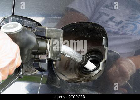 un uomo che rifornisce un'auto nera con carburante diesel in una stazione di servizio. Ugello di rifornimento vicino e getto di carburante. Foto Stock