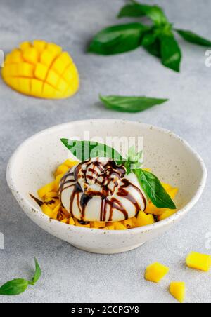 Burrata con tartare di mango con basilico verde e balsamico in un piatto bianco su fondo grigio di cemento. Colazione. App deliziosa Foto Stock