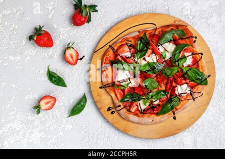 Pizza gourmet fatta in casa con salsa di pomodoro, fragole, burrata, basilico verde e balsamico. Vista dall'alto, messa a fuoco selettiva Foto Stock