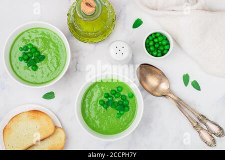 Zuppa di crema di piselli verde fatta in casa con menta in un piatto bianco su un tavolo di marmo. Piatto vegetariano (vegano) di verdure estive. Dieta sana. Selettivo Foto Stock