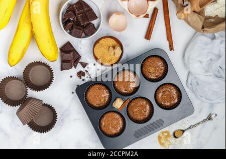 Preparazione di muffin fatti in casa con banana e cioccolato per la colazione. Ingredienti sulla tavola - farina di grano, uova, zucchero di canna, patatine di cioccolato, cres Foto Stock