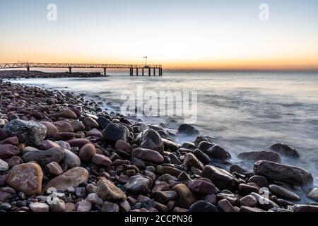 Alba da una spiaggia di ciottoli con un passaggio pedonale per il mare Foto Stock