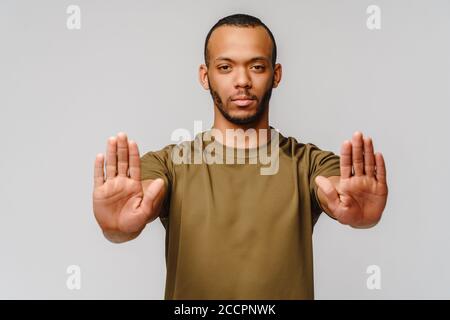 il giovane afro-americano gesturing SI FERMA con la mano sfondo grigio chiaro Foto Stock