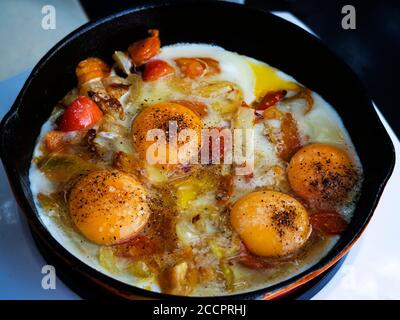 Le uova strapazzate con i pomodori vengono fritte in una padella di ghisa su una stufa elettrica di induzione Foto Stock