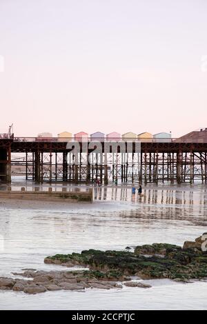 Colorate capanne sulla spiaggia su un molo a Hastings, Sussex est al tramonto con vista sul mare Foto Stock