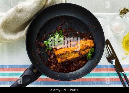 filetto di salmone rosa in salsa di pomodoro e cocco in padella antiaderente con prezzemolo su un tavolo con tovaglia di lino. cibo sano per la famiglia Foto Stock