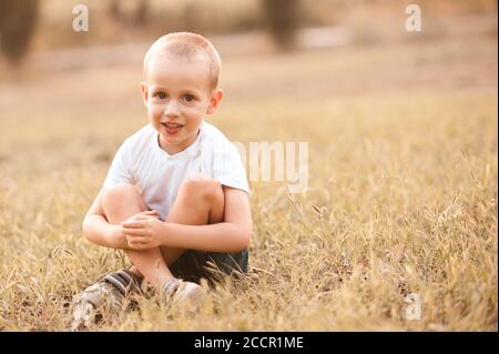 Carino ragazzo di 3-4 anni che indossa casual t-shirt bianca seduta in prato all'aperto. Infanzia. Foto Stock