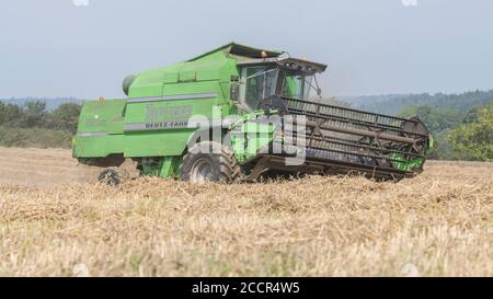 Mietitrebbia Deutz-Fahr 4065 che taglia il raccolto di grano 2020 nel Regno Unito nelle giornate estive calde e riempie l'aria di polvere. Aspo a denti e cabina operatore visibili. Grano britannico. Foto Stock