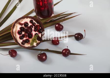 Dessert di panna montata e ciliegie fresche e ribes, succo di ciliegia con ghiaccio, foglie di palma su un tavolo bianco. Vista dall'alto. Copia spaes Foto Stock