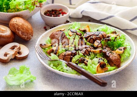 Insalata di lattuga calda con fegato di pollo, funghi fritti, olio d'oliva, condimenti e balsamico. Deliziosa cena gourmet. Messa a fuoco selettiva Foto Stock