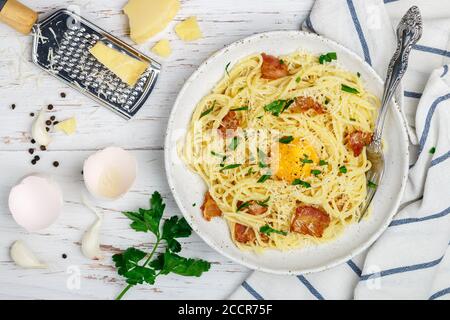 Pasta Carbonara. Spaghetti con pancetta, uova, prezzemolo e salsa di parmigiano in un piatto bianco su un tavolo di legno. Tradizionale mediterraneo (italiano) Foto Stock