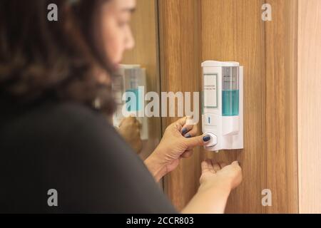 Donna lavando la mano con gel di alcol dopo aver utilizzato l'ascensore pubblico. Foto Stock