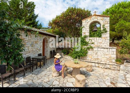 Una ragazza che legge nel cortile di una piccola chiesa greco-ortodossa in pietra, Meganissi, Isole IONIE, Grecia Foto Stock