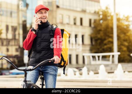 Courier Guy che parla sul telefono cellulare seduto in bicicletta all'aperto Foto Stock