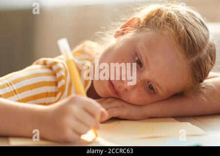 Ritratto dai toni caldi di cute foto di disegno di ragazza dai capelli rossi mentre si steso la testa sul tavolo sotto la luce del sole Foto Stock