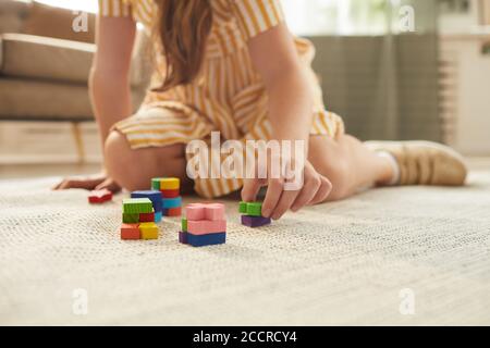 Primo piano dai toni caldi di una ragazza irriconoscibile che gioca con blocchi colorati mentre si siede sul pavimento in un accogliente interno, spazio di copia Foto Stock