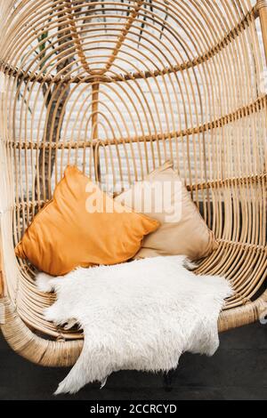 Sedia in rattan in vimini nel loft cafe. Arredamento eco-friendly stile e concetto. Cuscini arancioni e morbida pelliccia sulla sedia. Hipster Cafe in stile messicano con cactus e palme. Foto Stock