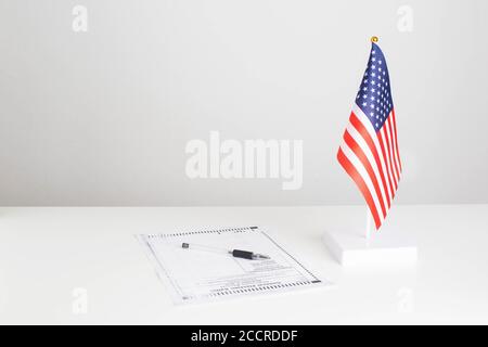 La penna e il documento elettorale per le elezioni presidenziali sono sul tavolo, la bandiera americana su sfondo bianco. Concetto DI elezione presidenziale DEGLI STATI UNITI Foto Stock