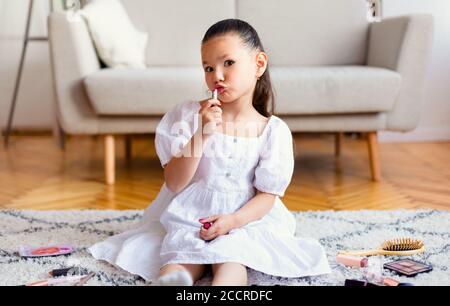 Little Girl Putting on Lipstick giocare con Mamma Cosmetics Indoor Foto Stock