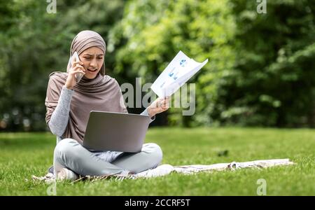 Arrabbiata donna araba freelance che lavora al parco, parlando al telefono Foto Stock