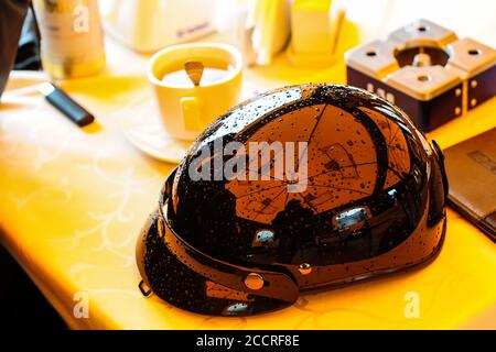 casco nero lucido per moto in stile vintage con corrimano su un tavolo in un caffè accanto ad una tazza di caffè Foto Stock