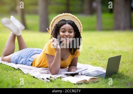 Bella ragazza nera che ha idea creativa durante i suoi studi con il laptop al parco, spazio libero Foto Stock