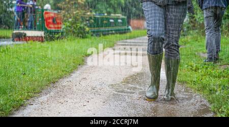 Vista frontale ravvicinata e dall'angolo basso delle pozze verdi indossate da una donna che spruzza attraverso le pozzanghere in caso di pioggia battente, Regno Unito, camminando lungo il canale cittadino. Foto Stock