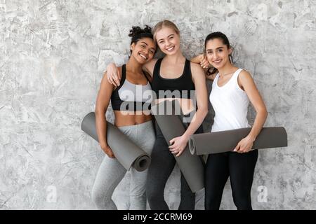 Concetto di fitness e sport. Ragazze multietniche con tappetini yoga in posa vicino alla parete Foto Stock