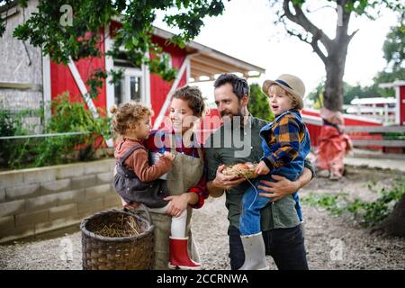 Ritratto di famiglia con bambini piccoli in piedi in fattoria, reggendo cestino con uova. Foto Stock