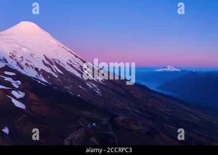 foto aerea dall'alta quota della vetta innevata del vulcano osorno nell'ora blu. Sullo sfondo il lago Todos los Santos e il Tronad Foto Stock