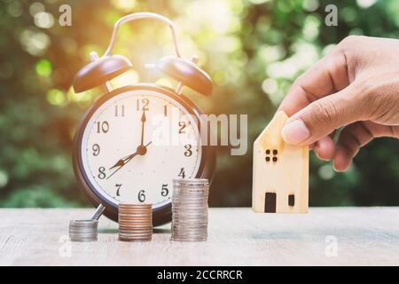 Primo piano del modello di casa di tenuta di mano maschio con sfondo bokeh verde risparmiando denaro per prepararsi per il futuro. Foto Stock